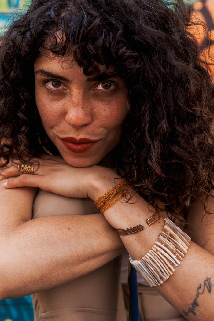 Close-up portrait of a woman with curly hair, wearing bracelets and resting her chin on her hands.