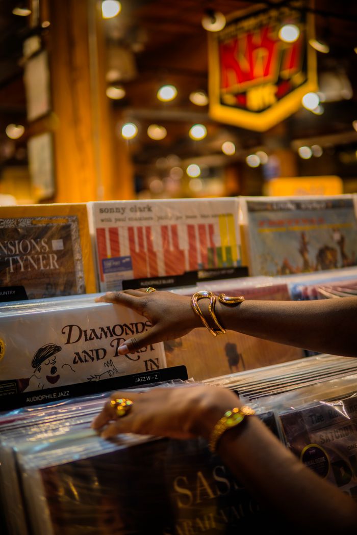 Person browsing vinyl records in a music store with warm, cozy lighting.