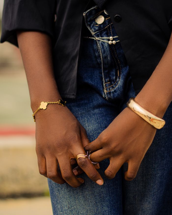 Close-up of hands with elegant bracelets and rings, denim jeans in background.