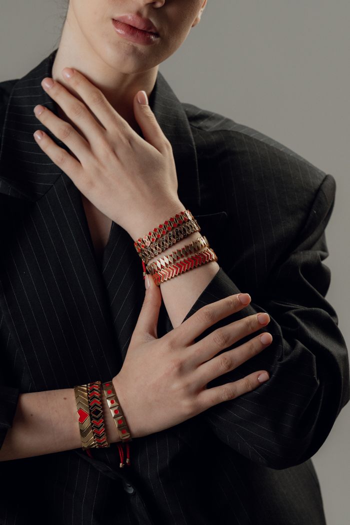 Close-up of a woman elegantly wearing colorful bracelets against a neutral background.