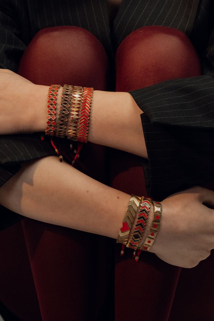 Close-up of a person's arms draped with stylish handmade bracelets in red and gold colors.