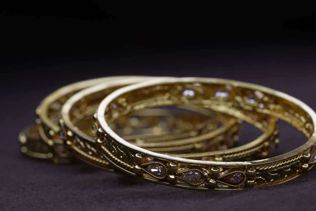 Elegant close-up of ornate gold bangles with gemstone accents on a dark surface.