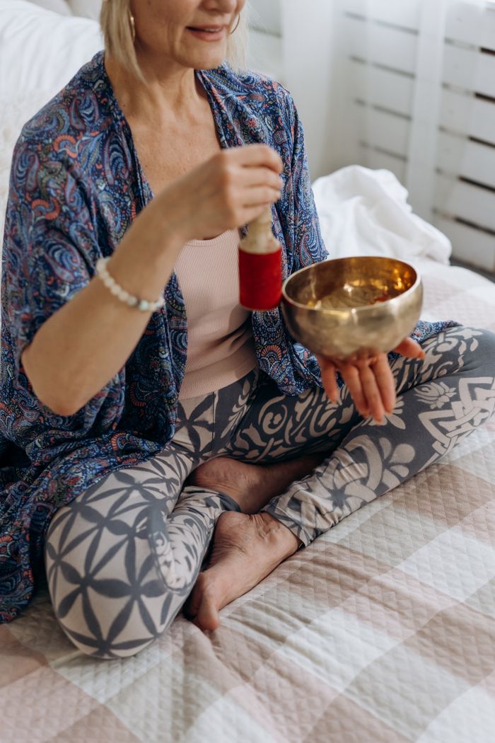 A woman practices meditation with a Tibetan singing bowl for relaxation and wellness indoors.